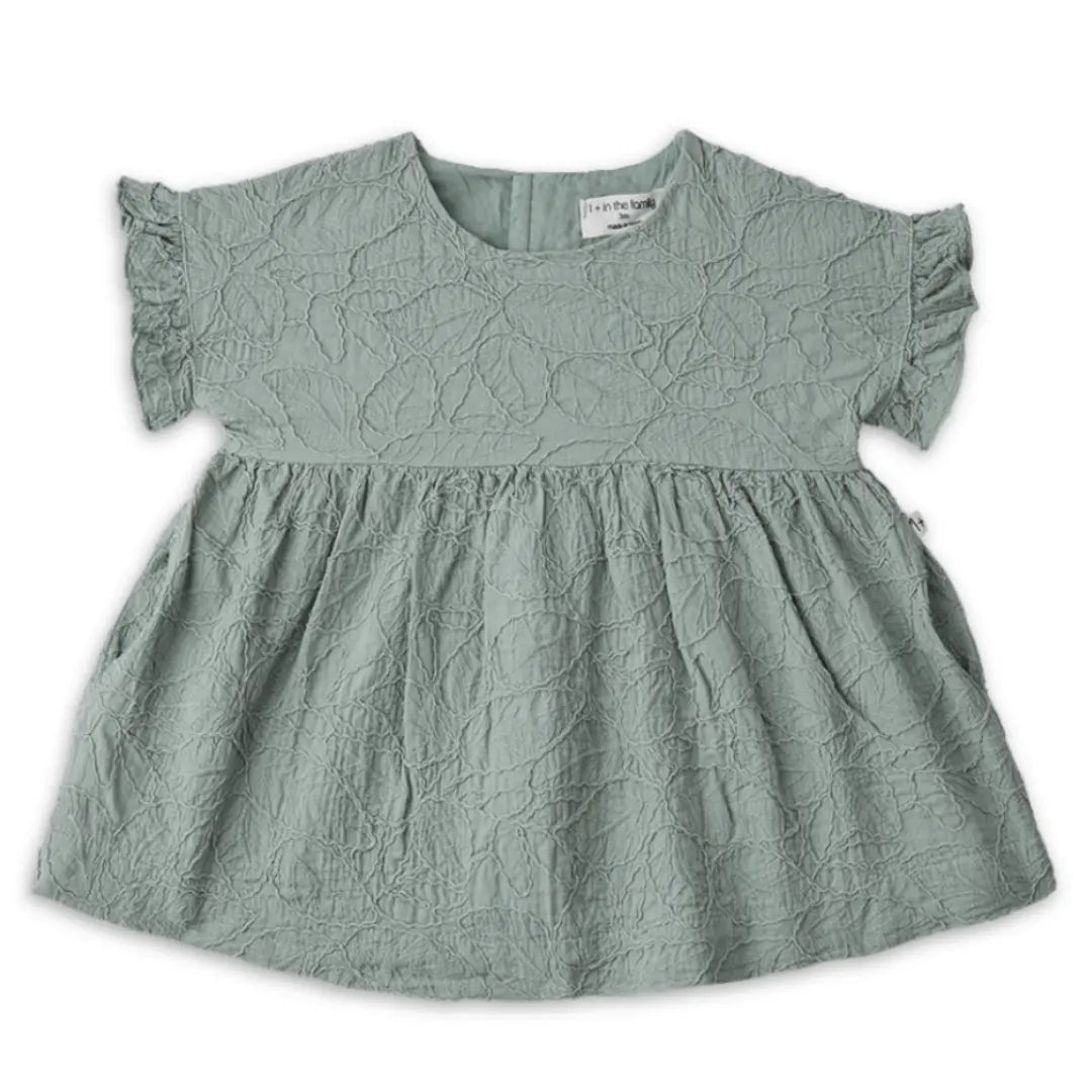 A sophisticated 1+ in the Family Satuna dress in a neutral textured fabric, showcasing its modern A-line silhouette and architectural drape.