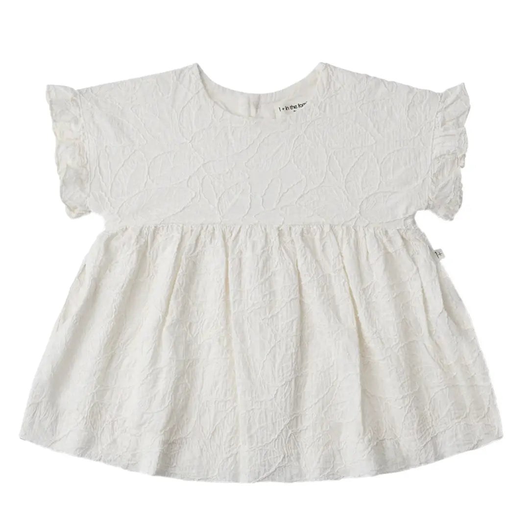 A sophisticated 1+ in the Family Satuna dress in a neutral textured fabric, showcasing its modern A-line silhouette and architectural drape.