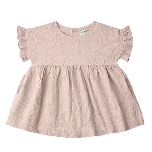 A sophisticated 1+ in the Family Satuna dress in a neutral textured fabric, showcasing its modern A-line silhouette and architectural drape.