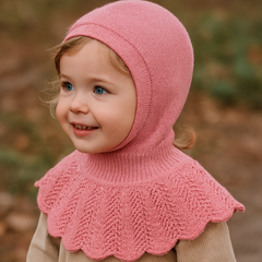 Child wearing a pink knitted hood and beige sweater outdoors