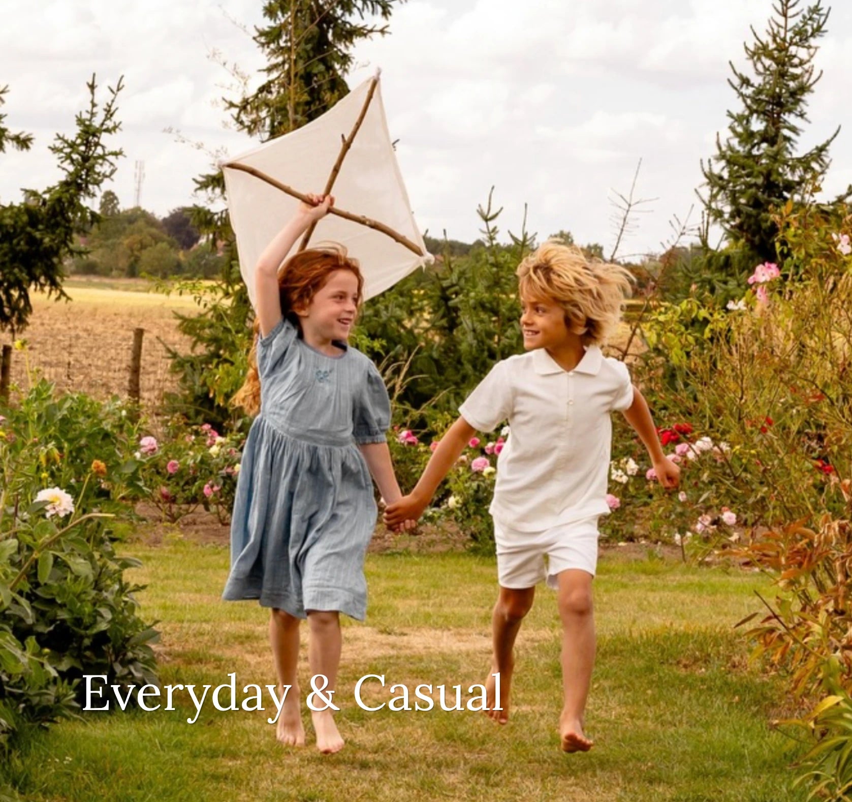 Two children running outdoors with a kite, surrounded by nature.