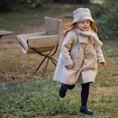 Child in a beige coat and hat running outdoors on a grassy area.