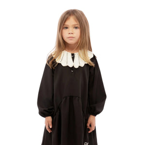 Young girl wearing a black dress with a white collar on a white background