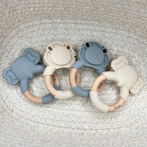 Four silicone baby teething rings in blue and beige on a textured surface