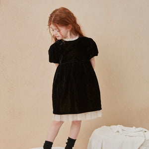 Young girl wearing a black velvet dress with a white lace trim on a beige background