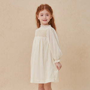 Young girl wearing a white dress with a textured bodice against a beige background