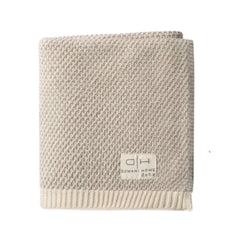 A folded beige textured knit blanket with a ribbed cream border and a small white brand label reading 'Domain Home Decor' on a plain white background.