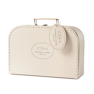 A cream-colored Domani Home Bebe suitcase-style bag with a top handle, decorative stitched edges, a small polka-dot pattern, and a hanging oval tag on a white background.