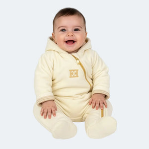 Baby wearing a cream-colored onesie with a logo on a white background