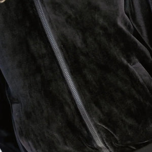 Close-up of a black velvet zip-up jacket showing the plush fabric texture and a dark zipper running diagonally across the frame.