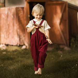 A child wearing the Lillies Dream beetroot suspender pants happily during an outdoor outing.