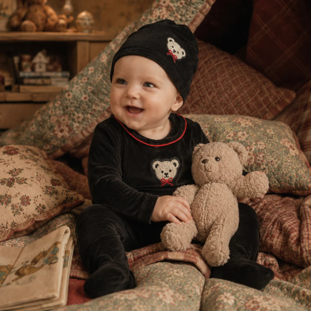 An infant resting peacefully while wearing the Little Label footie and hat set.