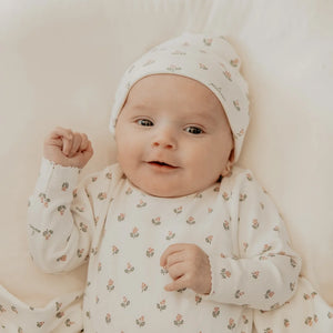 Baby wearing a floral outfit and hat on a soft surface