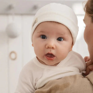 A newborn resting peacefully wrapped in the MarMar Copenhagen blanket and hat inside a luxury bassinet.