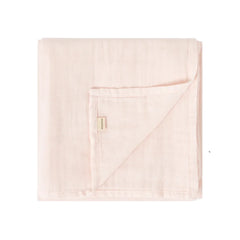 A folded light pink muslin blanket with a small beige brand tag, shown on a plain white background.