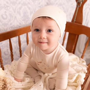 A newborn baby wearing the Mini Label ivory footie comfortably during a quiet nap.