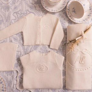 A newborn infant styled in the Mini Label cream knit footie set during a portrait session.