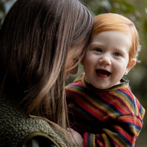 Woman holding a child wrapped in a colorful blanket outdoors