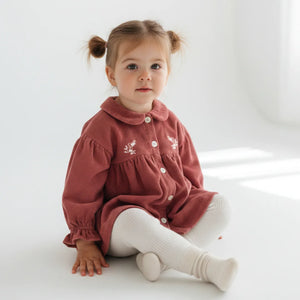 Young child wearing a red dress with white buttons on a white background