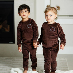 A child wearing the Pouf brown velour pajamas comfortably during a cozy morning at home.
