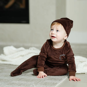 An infant resting comfortably while wearing the Pouf brown velour footie sleeper.