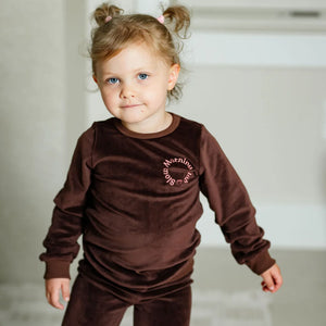 A child wearing the Pouf brown velour pajamas comfortably during a cozy morning at home