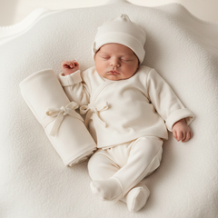 Newborn baby in a white outfit and hat lying on a white blanket