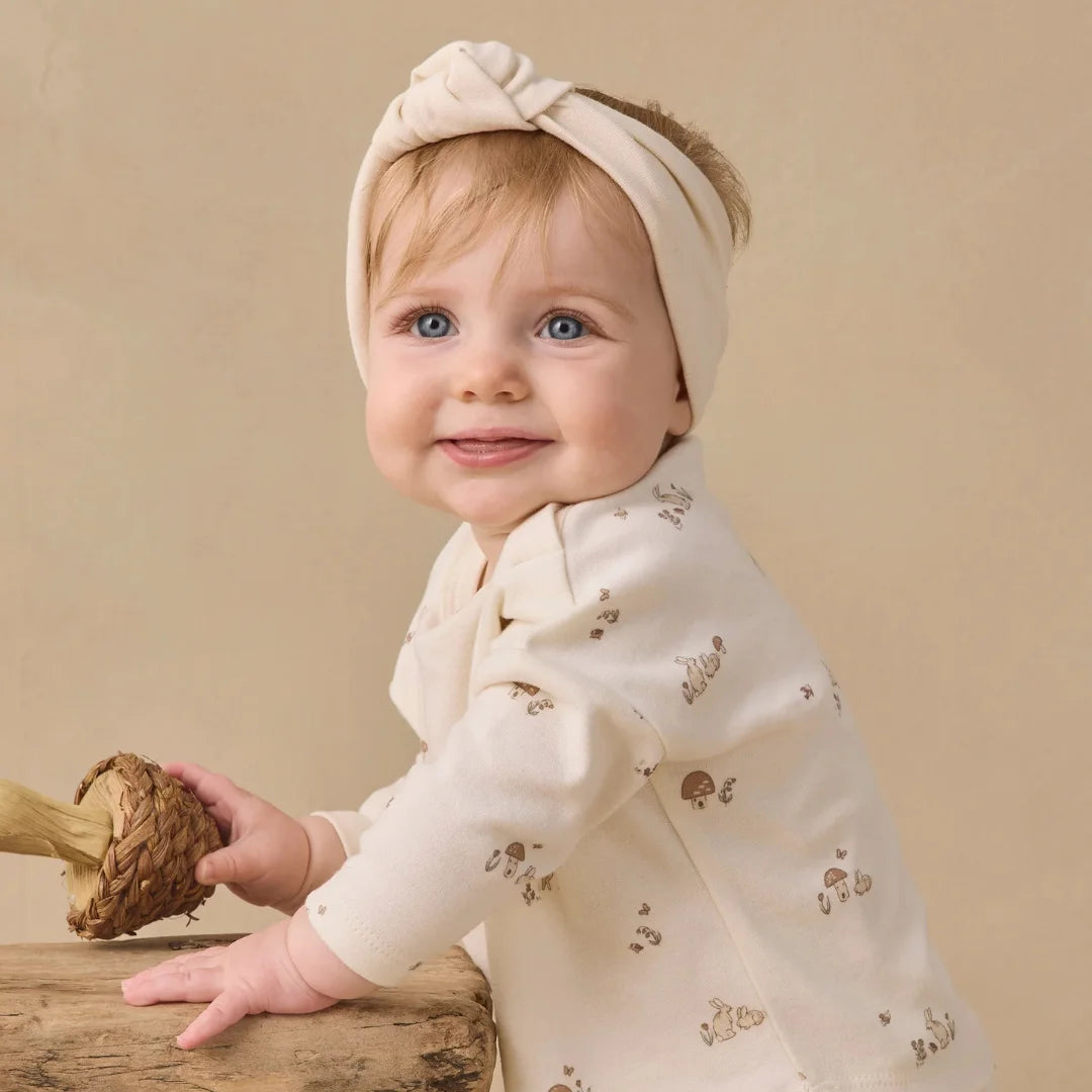 An infant wearing the Quincy Mae natural knotted headband comfortably during an outing.