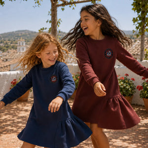 Two young girls in dresses running outdoors with a scenic background.