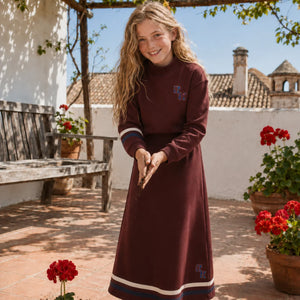 A teenage girl walking outdoors wearing the coordinated cranberry RetroKid top and skirt set.
