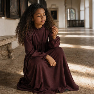 A young girl wearing the long, burgundy RetroKid Isla maxi sweater dress.