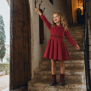A young girl happily playing while wearing the structured red RetroKid scuba dress.