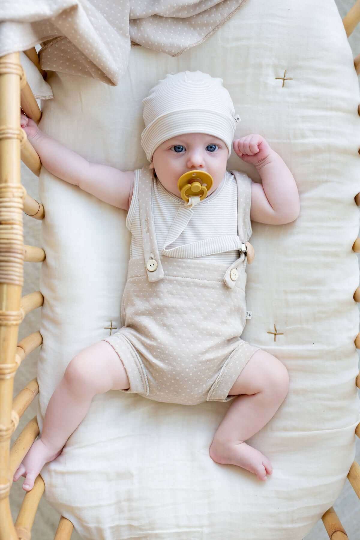 A pair of soft, beige 1+ in the Family baby bloomers featuring classic attached suspender straps on model