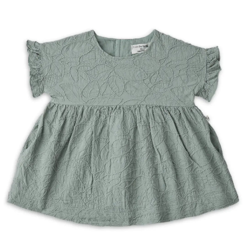 A sophisticated 1+ in the Family Satuna dress in a neutral textured fabric, showcasing its modern A-line silhouette and architectural drape.