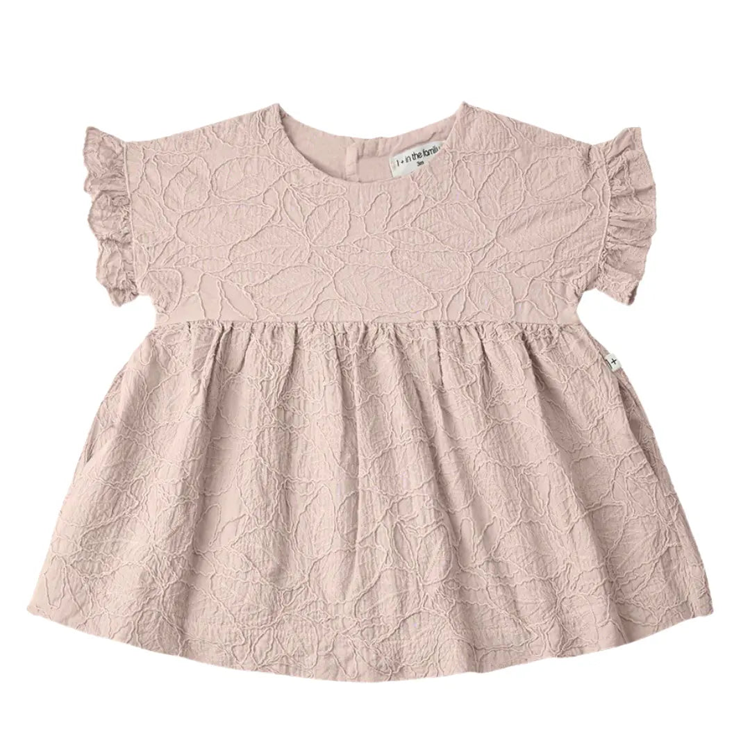A sophisticated 1+ in the Family Satuna dress in a neutral textured fabric, showcasing its modern A-line silhouette and architectural drape.