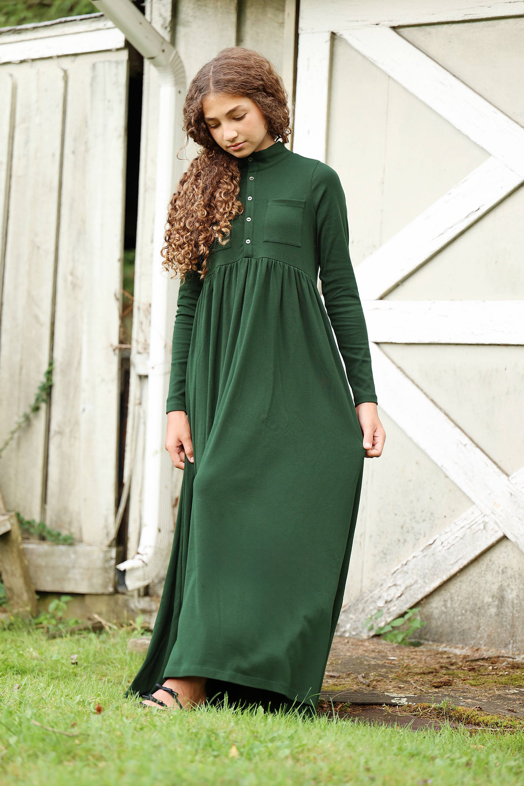 Girl wearing a green dress standing in front of a wooden building.