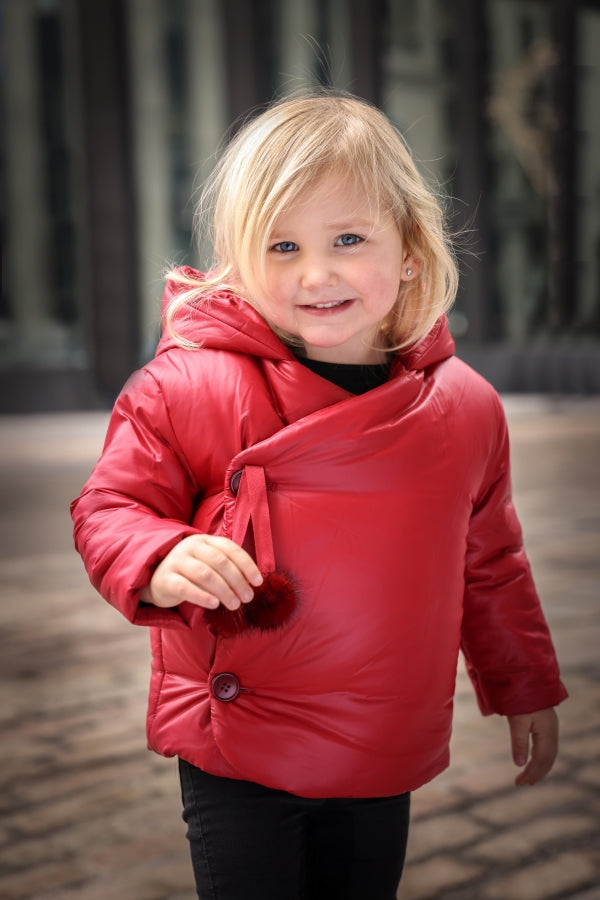 Child wearing a red puffer jacket outdoors on a blurred background