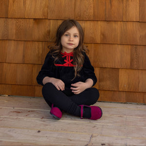 Young girl sitting on a wooden floor in front of a wooden wall with a round window.