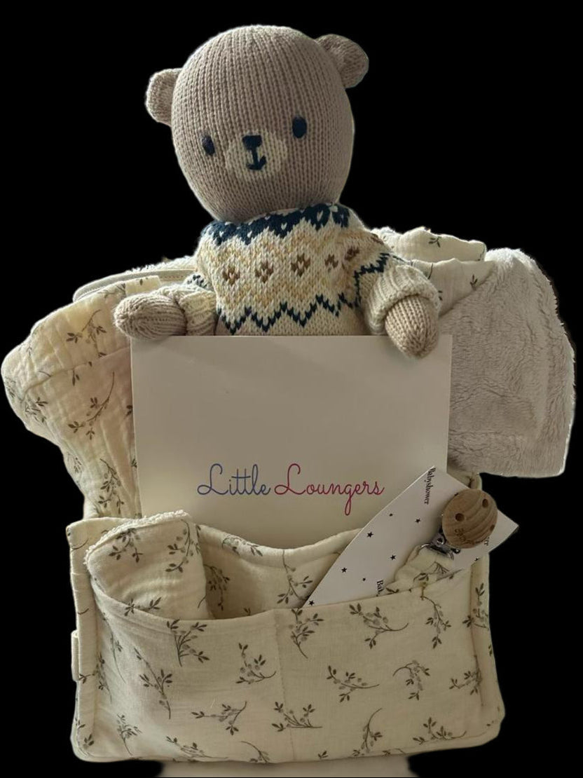 Teddy bear in a chair with a 'Little Loungers' card on a branded box in a store setting.