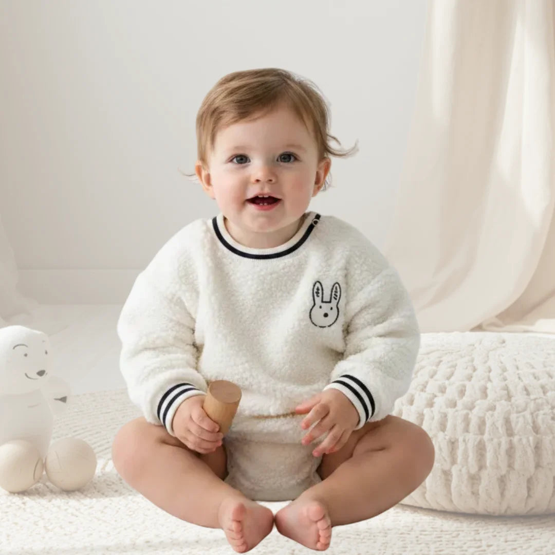 Child wearing a white sweater with a bunny design, sitting on a white surface.