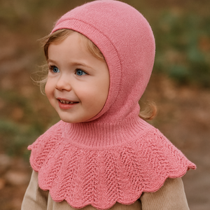 Child wearing a pink knitted hood and beige sweater outdoors
