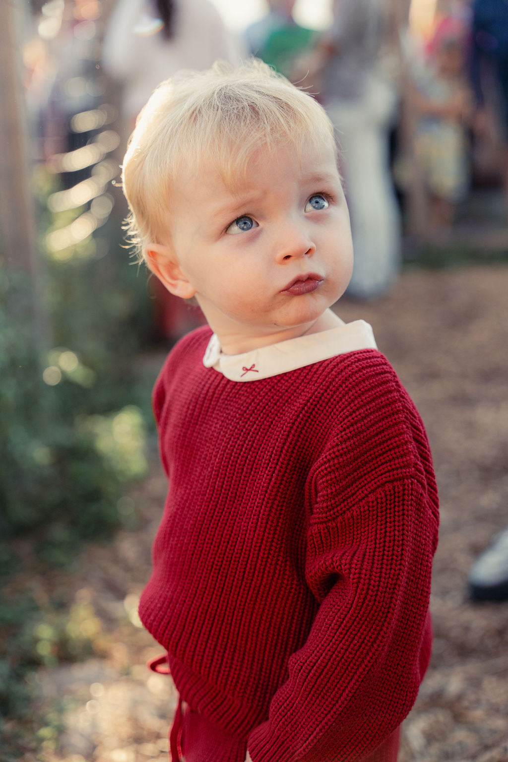 Child wearing a red sweater with a blurred outdoor background