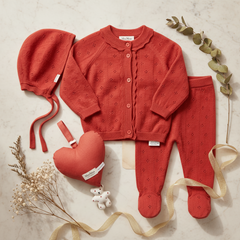 Red baby outfit set with cardigan, pants, hat, and heart-shaped rattle on a white background