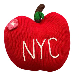 Red knitted apple-shaped pillow with 'NYC' embroidery on a white background