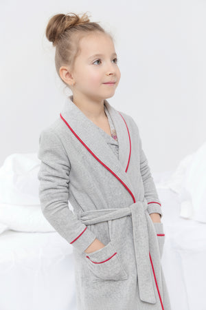 Child wearing a gray robe with red trim on a white background