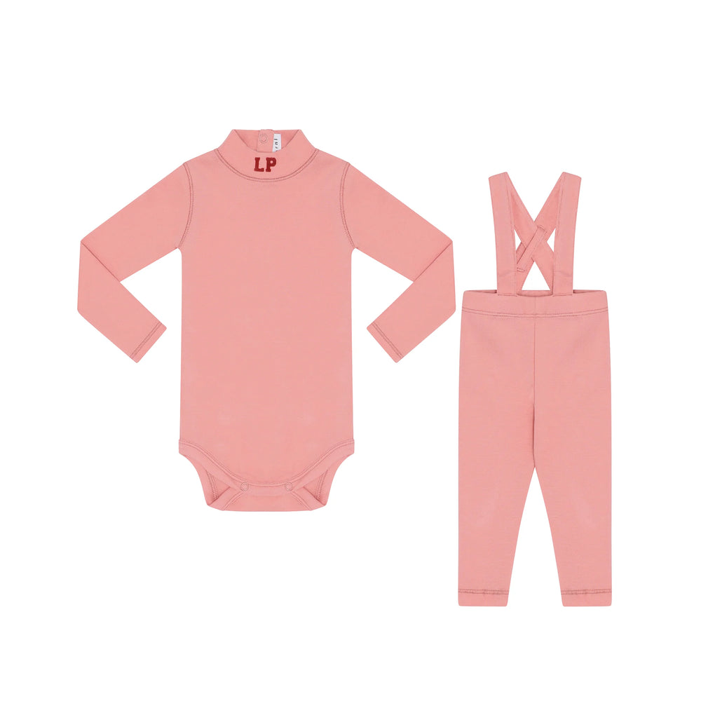 Pink baby onesie with long sleeves and pink pants with suspenders on a white background