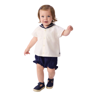 Child wearing a white shirt with navy trim and navy shorts on a white background