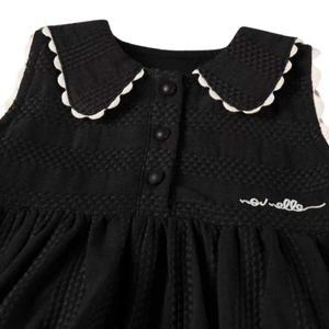 Black dress with white scalloped collar and buttons on a white background