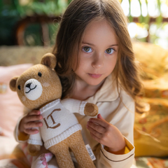 Young girl holding a teddy bear with a blurred outdoor background