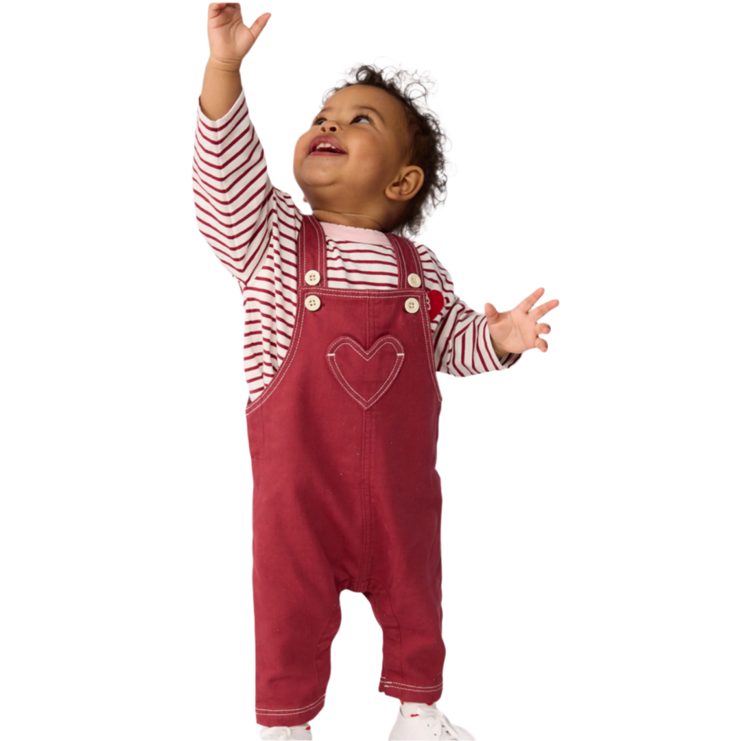 Child wearing red overalls with a heart design and a striped shirt on a white background